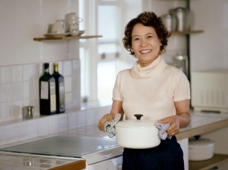 Woman standing in kitchen holding out a casserole dish