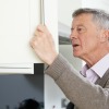 Elderly man looking in cupboard with perplexed expression