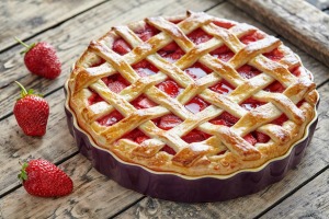 A baked strawberry pie and loose strawberries on wooden table