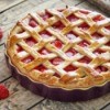 A baked strawberry pie and loose strawberries on wooden table