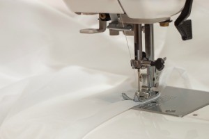 Close up of a sewing machine foot sewing white chiffon fabric