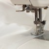 Close up of a sewing machine foot sewing white chiffon fabric