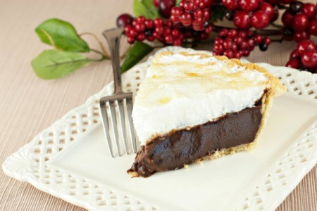 A slice of chocolate meringue pie with a very thin crust being served on a white plate