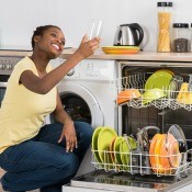 Woman smiling as she looks at a glass while she empties dishwasher