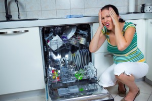 Woman making shocked face as she squats down next to open dishwasher