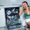 Woman making shocked face as she squats down next to open dishwasher