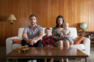 Family posed on sofa in front of wall with wood paneling