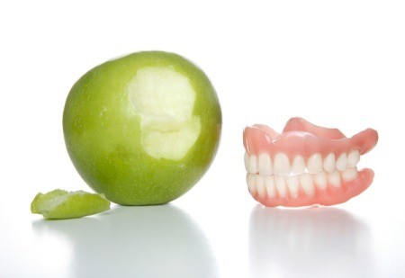 Apple with a bite next to it sitting next to a pair of dentures