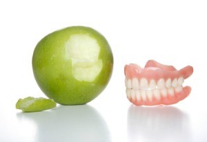 Apple with a bite next to it sitting next to a pair of dentures