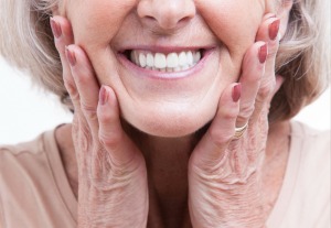 Close up of the mouth of a smiling senior woman with her hands on either side of her jaw