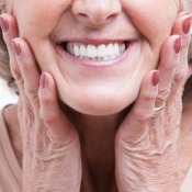 Close up of the mouth of a smiling senior woman with her hands on either side of her jaw