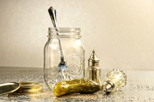 Pickle and old fashioned salt and pepper shakers next to an empty jar with a fork in it.