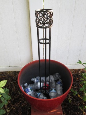 Flower pot filled part way with plastic bottles and with a wrought iron trellis in the center.