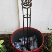 Flower pot filled part way with plastic bottles and with a wrought iron trellis in the center.