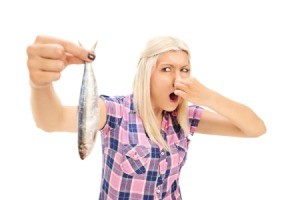 Woman holding a fish at arms length while holding her nose with the other hand