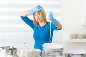 Woman with stacks of clean dishes squeezing soapy water from sponge with an overwhelmed expression