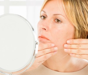 Woman looking in the mirror while touching her skin.