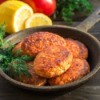 Salmon cakes in a cast iron pan with a sprig of dill.