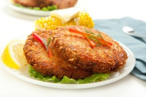 2 Fried salmon patties with a wedge of lime and a cob of corn.