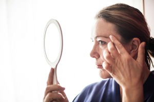 A woman looking at her face in a mirror.