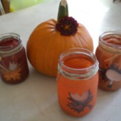 Three of the glass bottle candle holders arranged around a pumpkin.