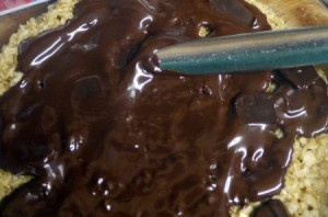 Chocolate being spread on top of a dessert.