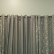 Grayish taupe curtains hanging against a neutral colored wall.