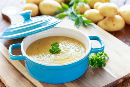 Bowl of potato soups surrounded by potatoes