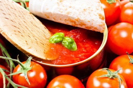 Wooden spoon dipping into can of tomato soup with basil.  Can is surrounded by tomatoes