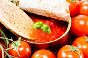 Wooden spoon dipping into can of tomato soup with basil.  Can is surrounded by tomatoes