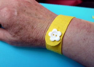 yellow felt wristband with white flower button on woman's wrist