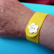 yellow felt wristband with white flower button on woman's wrist