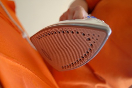 A clothes iron taking wrinkles out of orange fabric.