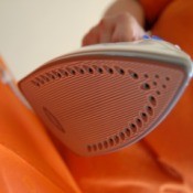 A clothes iron taking wrinkles out of orange fabric.