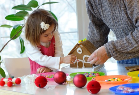 A toddler and her dad making a gingerbread house.
