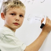 A boy writing on a white board with a dry erase marker.