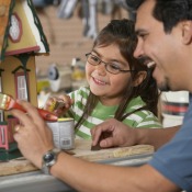 A father painting a dollhouse with his daughter.