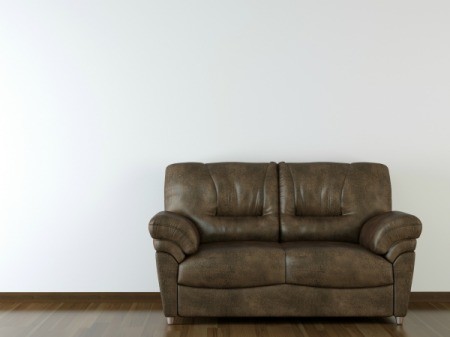 A brown leather sofa on a wood floor in front of a white wall.