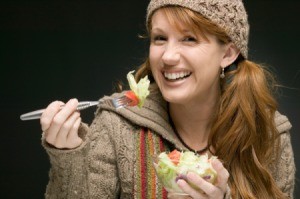 A woman eating a salad in a wool sweater.