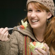 A woman eating a salad in a wool sweater.