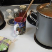 A coffee cup being used as a spoon rest on a stove.