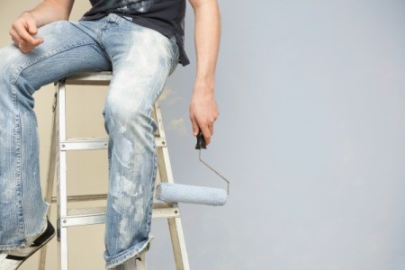 A man painting and wearing paint spattered jeans.
