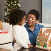 A grandmother helping her granddaughter make a gingerbread house.