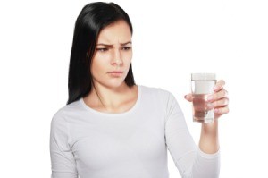 A woman looking concerned at a glass of water.