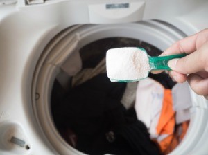 A person adding soap to a washing machine full of clothes.