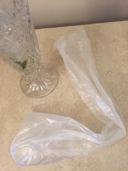A plastic bag from a newspaper next to a glass vase.