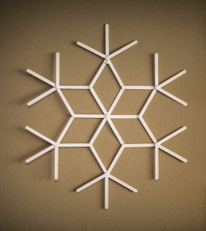 A finished popsicle stick snowflake, painted white.