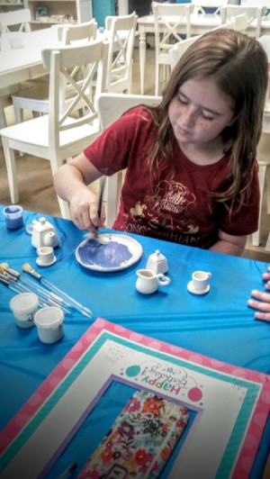 A girl painting a piece of pottery at a birthday event.