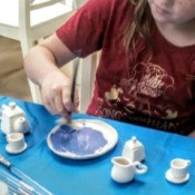 A girl painting a piece of pottery at a birthday event.