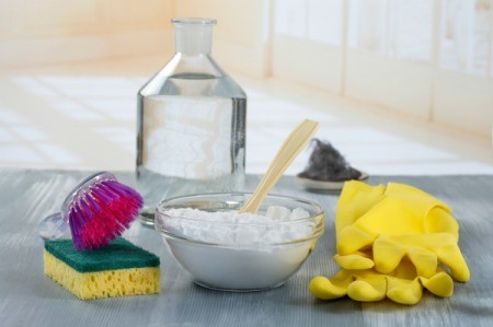 A bowl of baking soda with rubber gloves and sponge on a kitchen counter.